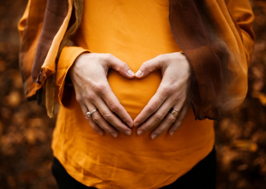 Schwangere Frau formt mit ihren Händen ein Herz über ihrem Bauch für den Eltern-Kind-Pass