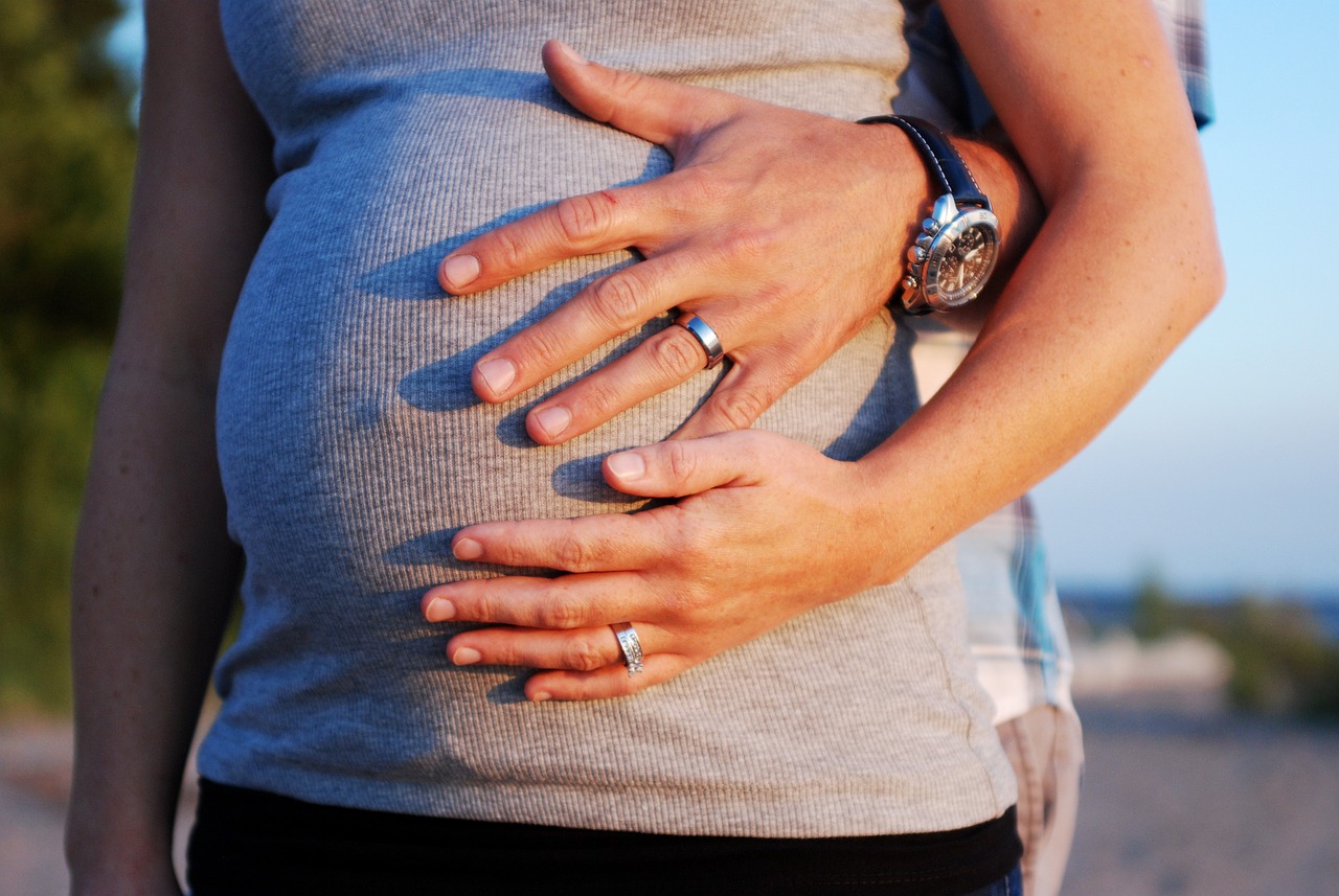 Eine Frau bei der Schwangerschaftsgymnastik mit Händen ihres Partners um ihren Bauch